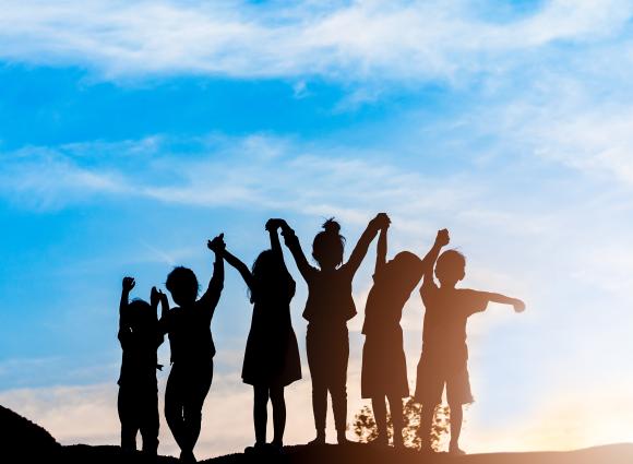 Group of people holding hands in front of a sunset